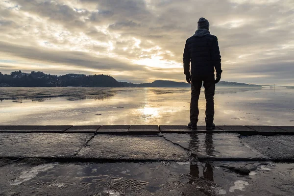 Uomo in piedi sulla riva, guardando il mare calmo. Riflessioni dell'uomo nel ghiaccio a terra. Nebbia e nebbia. Hamresanden, Kristiansand, Norvegia — Foto Stock