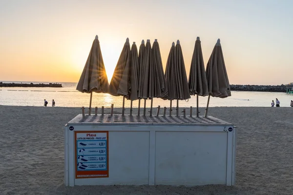 Napernyők bérelhetők, a népszerű Amadores strandtól. Naplemente és a strand, a háttérben. Amadores, Gran Canaria, Spanyolország — Stock Fotó