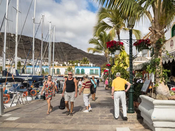 Puerto de Mogan, Gran Canaria in Spain - December 16, 2017: Tourists walking on the promenade in Puerto de Mogan, sailboats in the background. — Stock Photo, Image