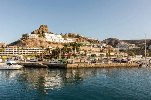 Puerto Rico, Gran Canaria - December 12 2017: Marina of Puerto Rico, a very popular travel destination. Boats, cars and people in the harbor. Hotels in the background. — Stock Photo, Image