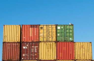 Kristiansand, Norway, November 5, 2017: Stack of containers at the container port in Kristiansand. Yellow, red, green and orange. Blue sky, a gull sitting on top of containers clipart