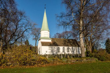 Beyaz ahşap kilise yan, ağaçlar, otlar ve mavi gökten sonbahar, Kristiansand, Norveç gördüm