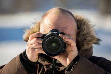 Norveç, 3 Şubat 2018: kış giyim erkek bir fotoğrafçı Canon 24-70 mm 2,8 L II lens ile Canon Kamera tutuyor. Alanında, karlı kış açık havada sığ derinliği.