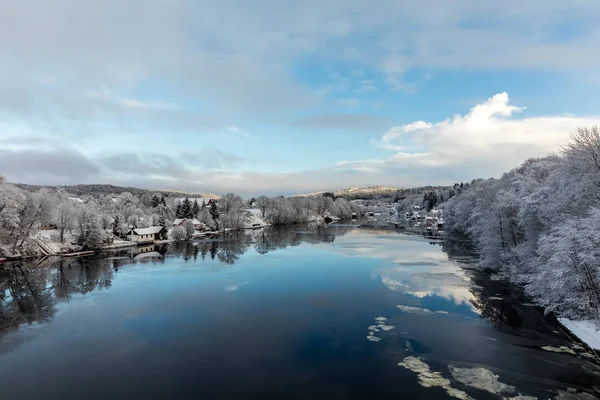 Kristiansand, Noruega - 17 de enero de 2018: Vista panorámica del río Tovdal en Tveit, con casas a orillas del río. Invierno, nieve en los árboles. Hielo flotando en el agua, reflejos del cielo . — Foto de Stock