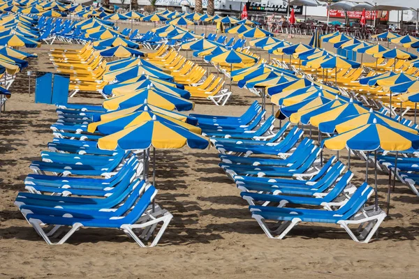 Filas de tumbonas azules con sombrillas azules y amarillas en la playa Playa de Puerto Rico en la Isla Canarias —  Fotos de Stock