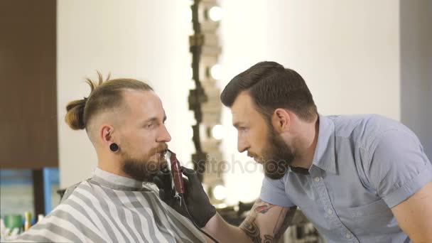 Conseguir una forma perfecta. Vista lateral de cerca del corte de pelo de barba de hombre joven barbudo por peluquería en la barbería — Vídeos de Stock