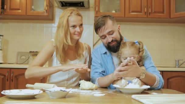 Feliz familia madre, padre e hija pequeña en la cocina preparando pasteles de la prueba . — Vídeo de stock