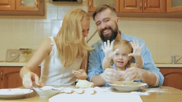 Feliz familia madre, padre e hija pequeña en la cocina preparando pasteles de la prueba . — Vídeos de Stock