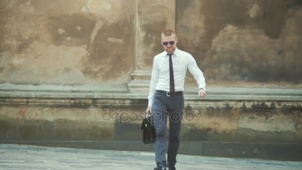 Un hombre de negocios serio con un maletín frente a un edificio de oficinas arreglando su corbata — Vídeo de stock