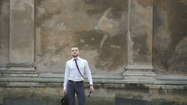 Serious businessman with a briefcase in front of an office building fixing his tie — Stock Video