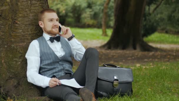 Hombre en un parque verde hablando por teléfono — Vídeo de stock