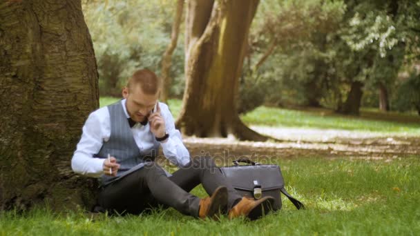 Jeune homme d'affaires est assis sous l'arbre — Video