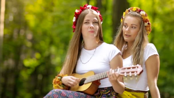 Två unga flickor med gitarr i en sommar skog — Stockvideo