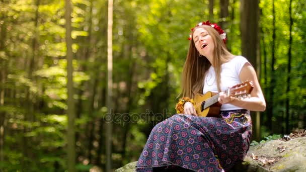 Romantisk flicka i en krans av vilda blommor reser med sin gitarr. Sommar. — Stockvideo