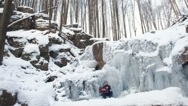 Happy young man playing the harmonium on a frozen waterfall — Stock Video