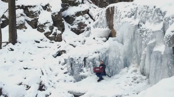 Glücklicher junger Mann spielt Harmonium auf einem gefrorenen Wasserfall — Stockvideo