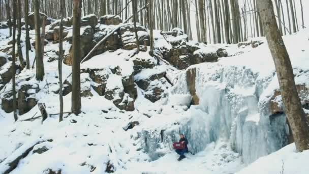 凍った滝で、ハルモニウムを遊んで幸せな若い男 — ストック動画