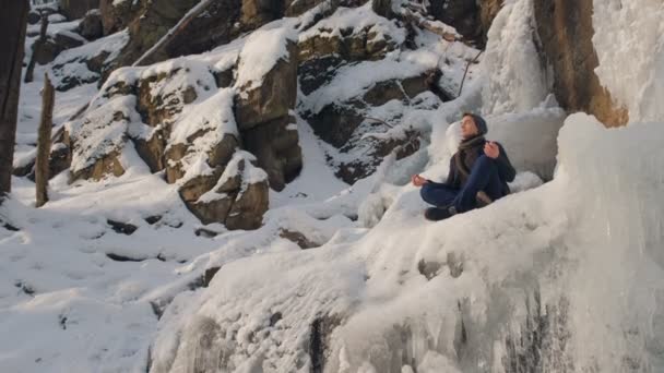 Портрет молодой человек, сидящий в медитации зимней реки — стоковое видео