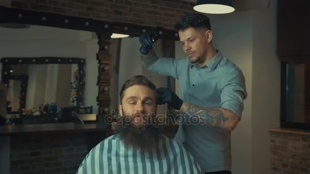 Молодий красивий перукар робить стрижку привабливого бородатого чоловіка в перукарні — стокове відео