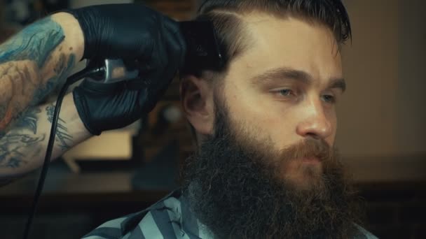 Joven peluquero guapo haciendo corte de pelo de hombre barbudo atractivo en la barbería — Vídeos de Stock