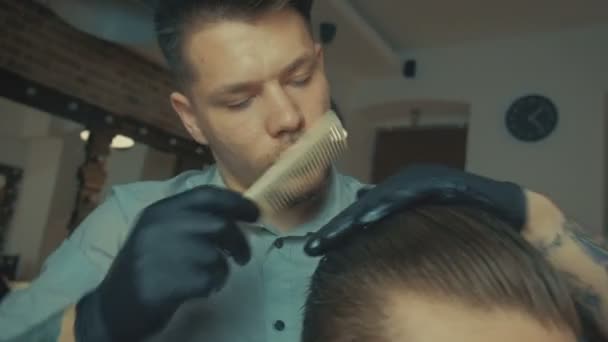 Atractivo hombre de pelo oscuro con camisa blanca haciendo un corte de pelo con secador de pelo y cepillo para el hombre mirando a la cámara . — Vídeos de Stock