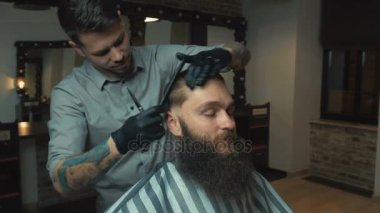Siyah saçlı ve beyaz gömlek ve siyah eldiven makas kuaför dükkanında ile acımasız istemci için bir saç kesimi yapıyor dövme ile berber