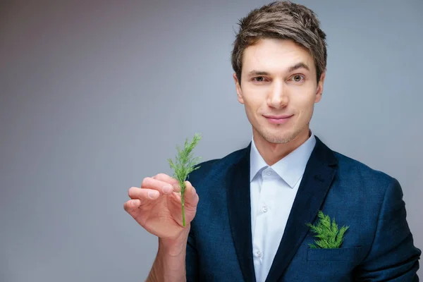 beautiful young attractive man in a blue business suit and white shirt in a studio with green fennel in hand and in your pocket