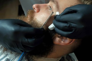 Genç sakallı adam Kuaför tarafından düz kenarlı ustura ile tıraş yakın çekim yan görünüm