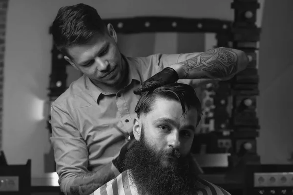 Красивый бородатый мужчина смотрит вперед, когда парикмахер стрижет его в парикмахерской — стоковое фото