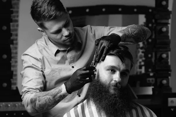 Knappe bebaarde man kijkt uit terwijl het hebben van zijn haren knippen door Kapper in de barbershop — Stockfoto