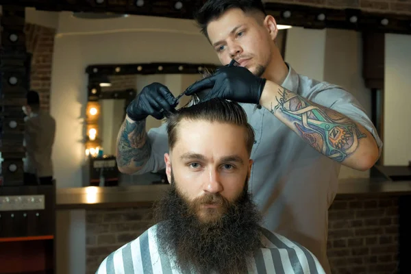 Knappe bebaarde man kijkt uit terwijl het hebben van zijn haren knippen door Kapper in de barbershop — Stockfoto