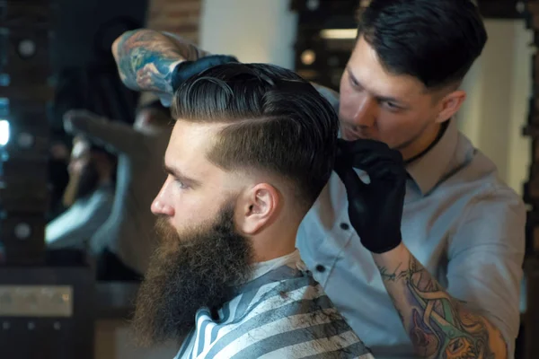 Knappe bebaarde man kijkt uit terwijl het hebben van zijn haren knippen door Kapper in de barbershop — Stockfoto