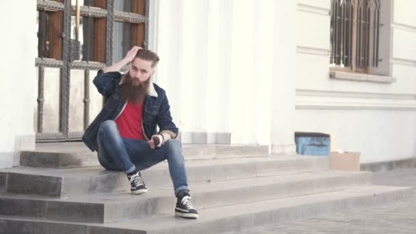 Handsome young stylish hipster man with long beard in grey shirt standing outdoor. Denim style — Stock Video