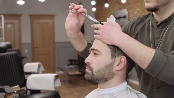 Мужчина парикмахер делает стрижку бороды взрослых мужчин в мужской парикмахерской. Стрижка с ножницами — стоковое видео