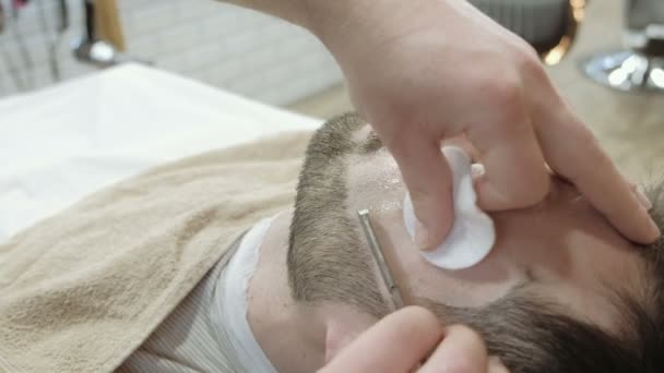 Retrato de cerca de un joven guapo afeitándose la barba con una navaja de afeitar. Concéntrate en la hoja — Vídeos de Stock