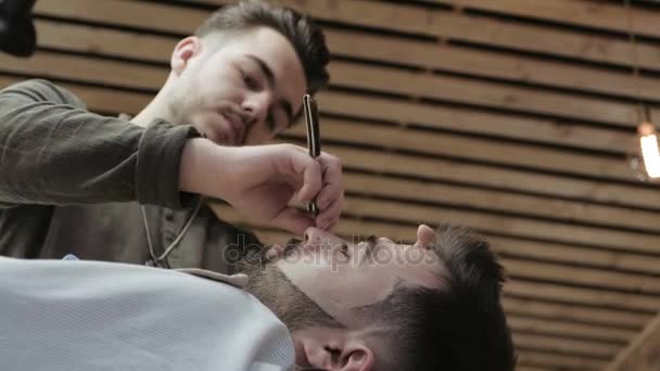 Close-up portrait of handsome young man getting beard shaving with straight razor. Focus on the blade — Stock Video