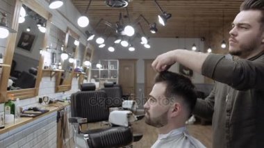 Yakışıklı sakallı adam kuaförde saçını kestirirken gülümsüyor.