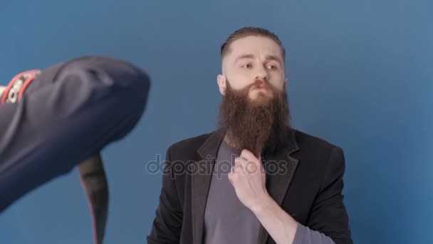 Фотограф фотографує чоловічу модель в студії з синім фоном. Хлопець модель з довгою бородою. Каталог зйомок моди — стокове відео