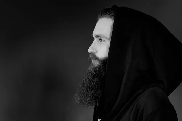 Retrato de homem sério elegante bonito em um capuz. Brutal homem com barba sobre fundo preto — Fotografia de Stock