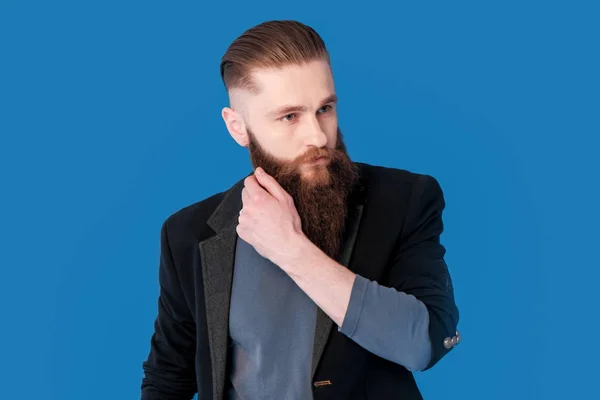 Retrato de um homem barbudo vestido com jaqueta preta e jeans no fundo azul e branco — Fotografia de Stock