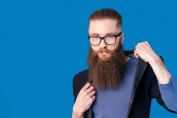 Prendre la vie au sérieux. Portrait de beau jeune homme en coffret ajustant ses lunettes tout en se tenant debout sur fond gris — Photo