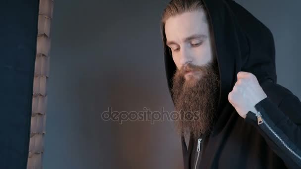 Retrato de homem sério elegante bonito em um capuz. Brutal homem com barba sobre fundo preto — Vídeo de Stock