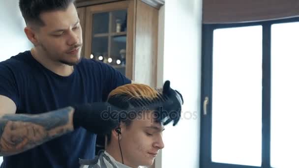 Jonge kerel, tiener, in de schoonheidssalon. Na verloop van het creëren van kapsel. Professionele kapper verven haar van haar cliënt. — Stockvideo