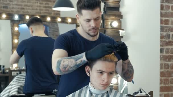 Junger Kerl, Teenager, im Schönheitssalon. im Prozess der Erstellung von Frisur. professionelle Friseurin färbt Haare ihres Kunden. — Stockvideo