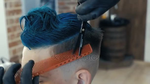 Peluquero cortar el pelo con tijeras y peine, un cliente es un joven hombre caucásico. Pelo azul brillante . — Vídeo de stock