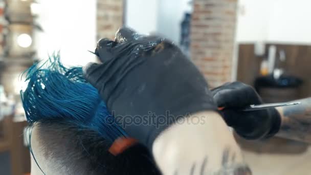 Kapper knippen van de haren met een schaar en kam, is een client een jonge blanke man. Helder blauwe haren. — Stockvideo