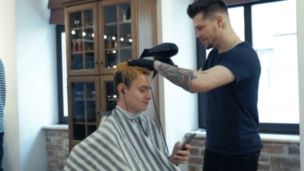 Jonge kerel, tiener, in de schoonheidssalon. Na verloop van het creëren van kapsel. Professionele kapper verven haar van haar cliënt. — Stockvideo