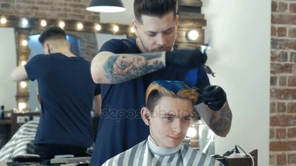 Ung kille, tonåringen, i skönhetssalong. Färd med att skapa frisyr. Professionell frisör färga håret på hennes klient. — Stockvideo