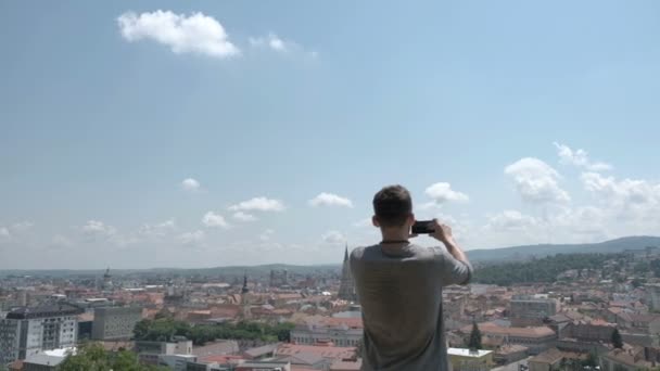 Чоловічий мандрівник зробити панорамне фото старого міста на свій телефон для Instagram або інших соціальних мереж. Поїздки в Румунії. — стокове відео