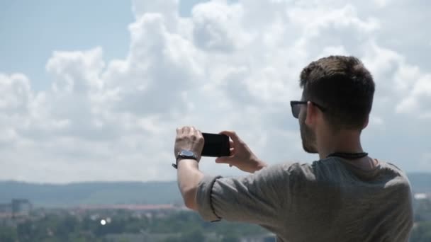 Мужчина-путешественник делает панорамное фото старого города на свой телефон для Instagram или других социальных сетей. Поездка в Румынию. Закрыть — стоковое видео
